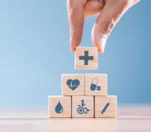 a person placing a small wooden block on a stack of other wooden blocks, all of which have small health logos on them