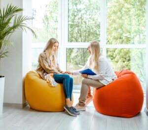 two blonde women sitting on beanbag chairs, one comforting the other, symbolising mental health coverage in business