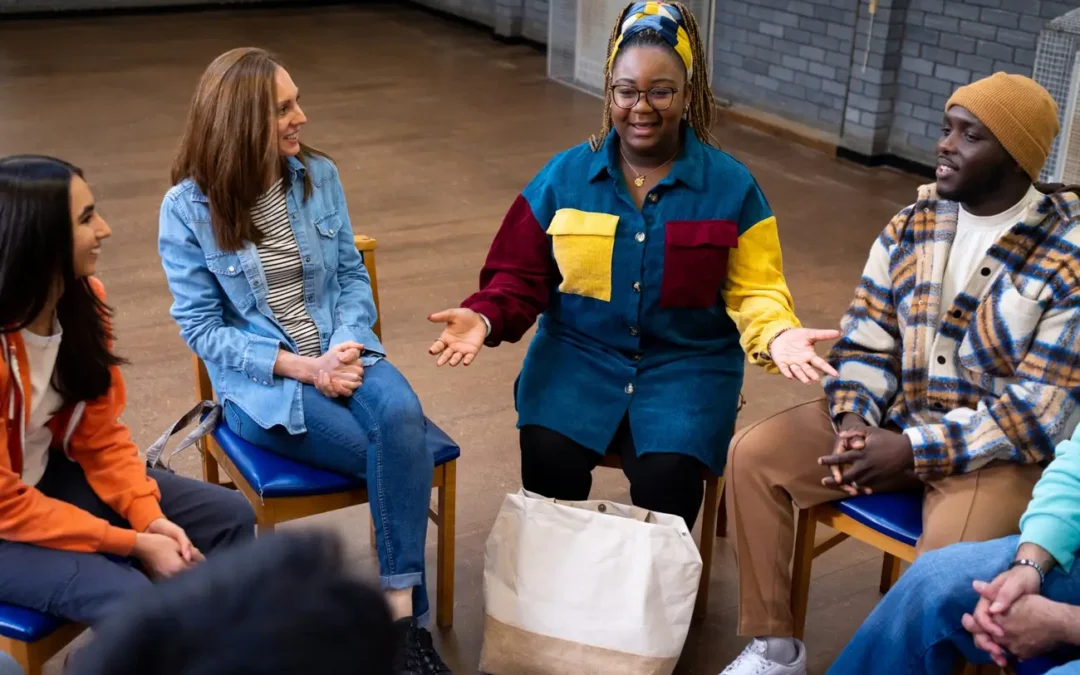 a group of people sitting in a circle of chairs, similar to a support group