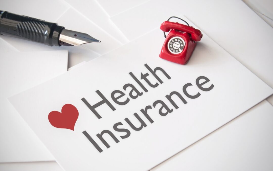 a calligraphy pen, a tiny red rotary phone, and a piece of paper that says "health insurance"