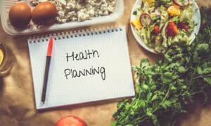 a notebook and pen that says  "health planning" surrounded by healthy foods, like eggs and a salad