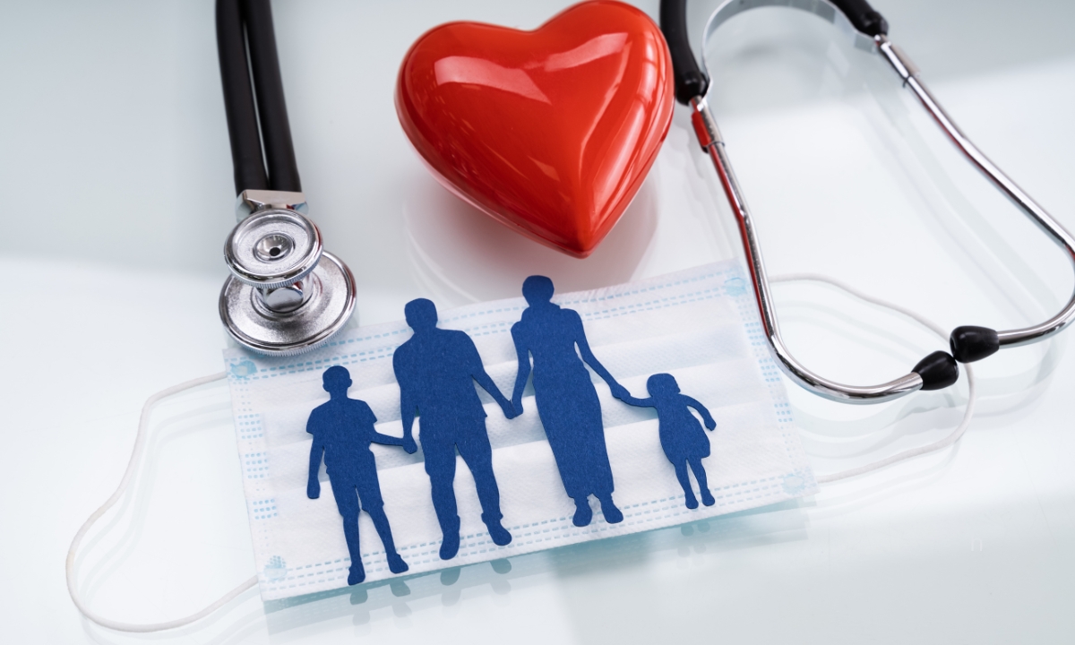 a family's silhouette in cardstock on top of a covid mask with a small red wooden heart and a stethoscope 