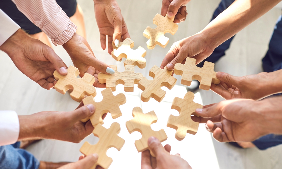 a group of people's hands putting wooden jigsaw pieces in the middle of the circle